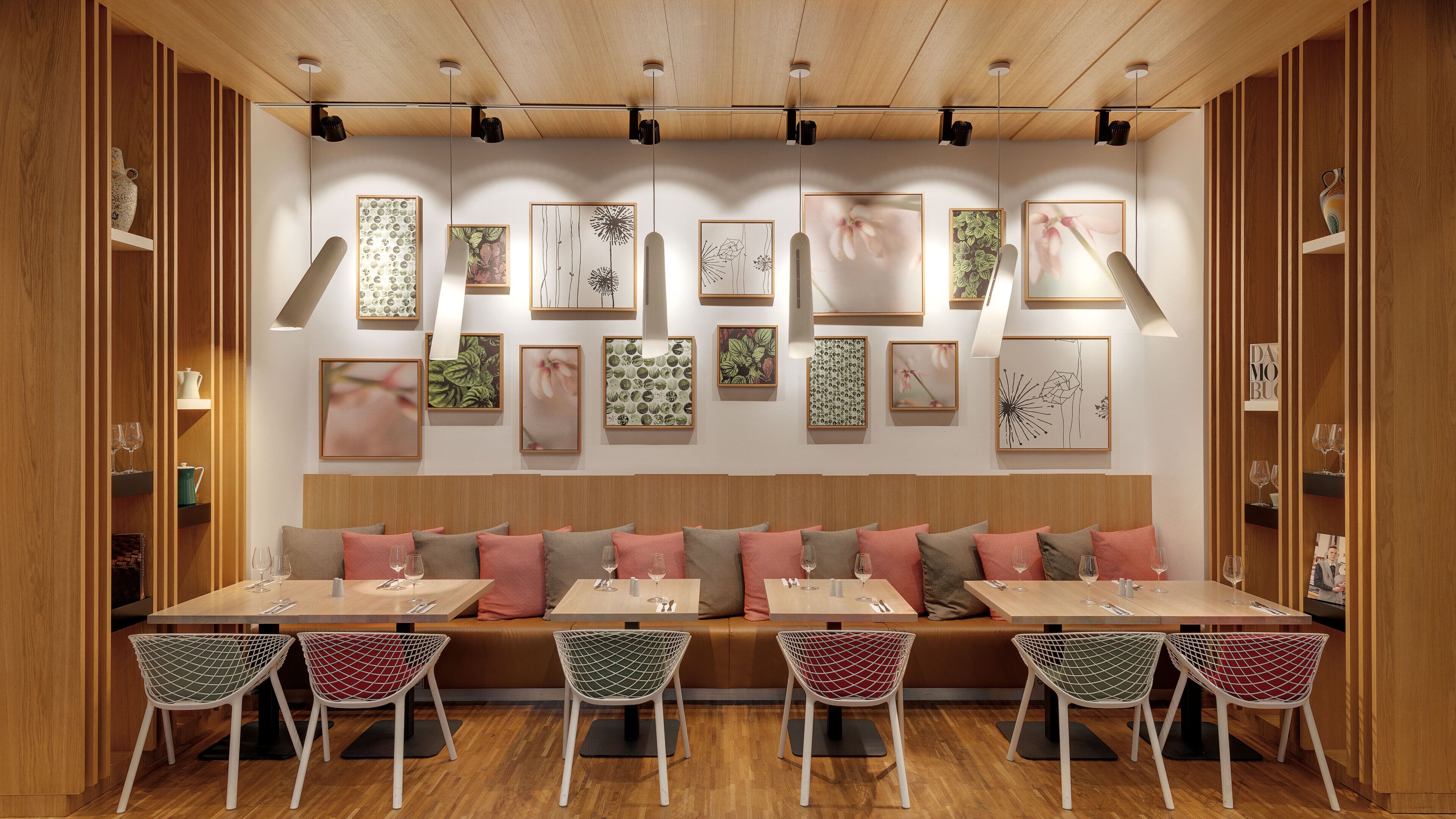 Un restaurante con un largo banco de madera, sillas de malla blanca y una pared decorada con obras enmarcadas.