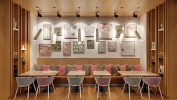 A restaurant with a long wooden bench, white mesh chairs, and a wall adorned with framed artwork.