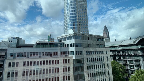 Ein modernes Hochhaus mit einem zylindrischen Glasturm, umgeben von anderen zeitgenössischen Gebäuden.
