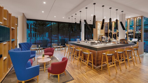 A modern bar area with a central counter, bar stools, and seating with round tables. - Holiday Inn Frankfurt - Alte Oper by IHG (Frankfurt)