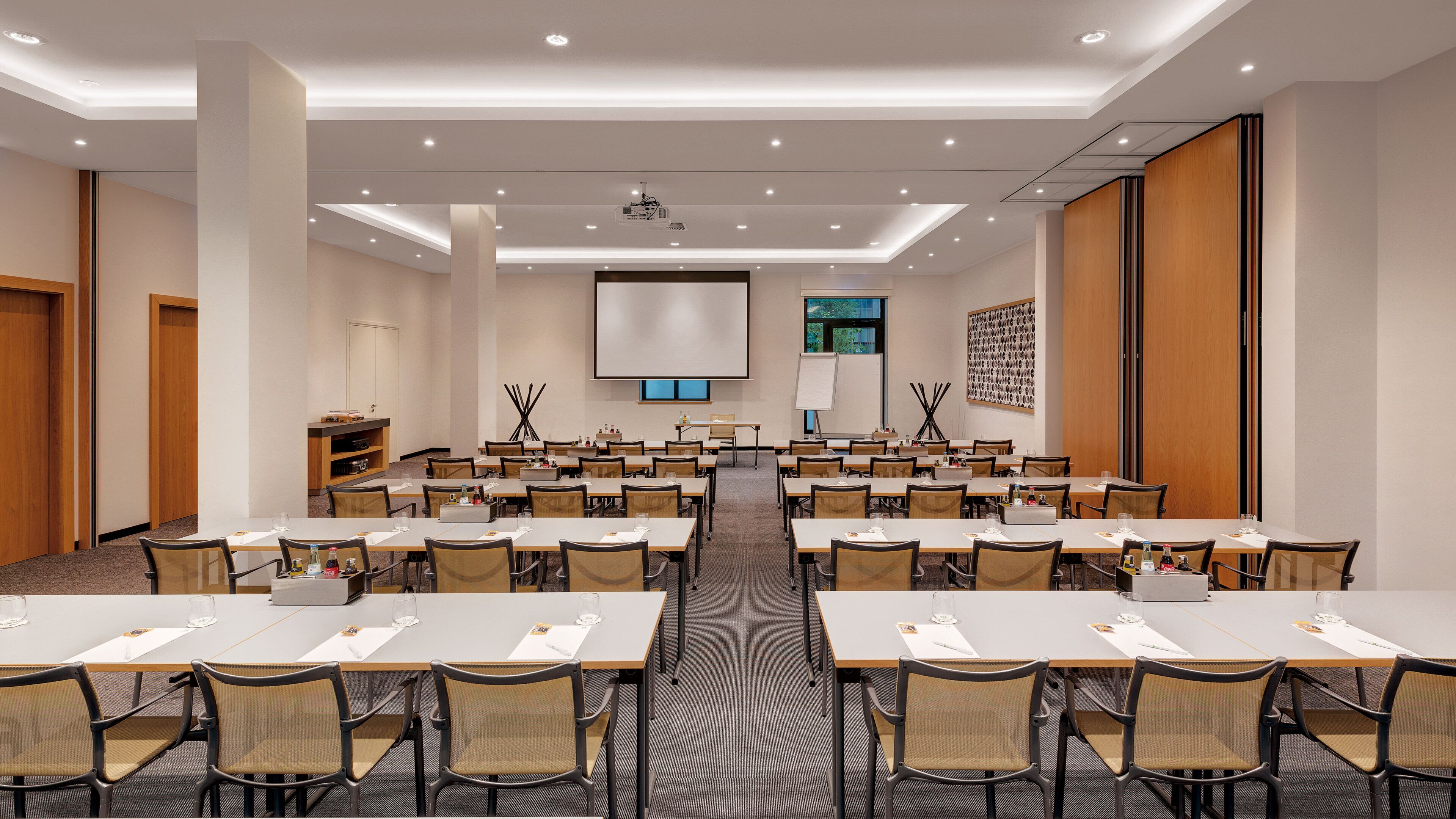 A conference room with multiple tables and chairs, a projector screen, and a whiteboard.