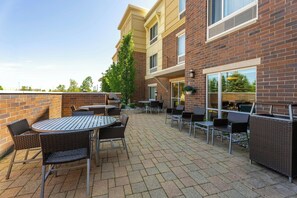 A patio area with outdoor seating, a brick building, and a view of the surrounding landscape. - TownePlace Suites Detroit Auburn Hills (Auburn Hills)