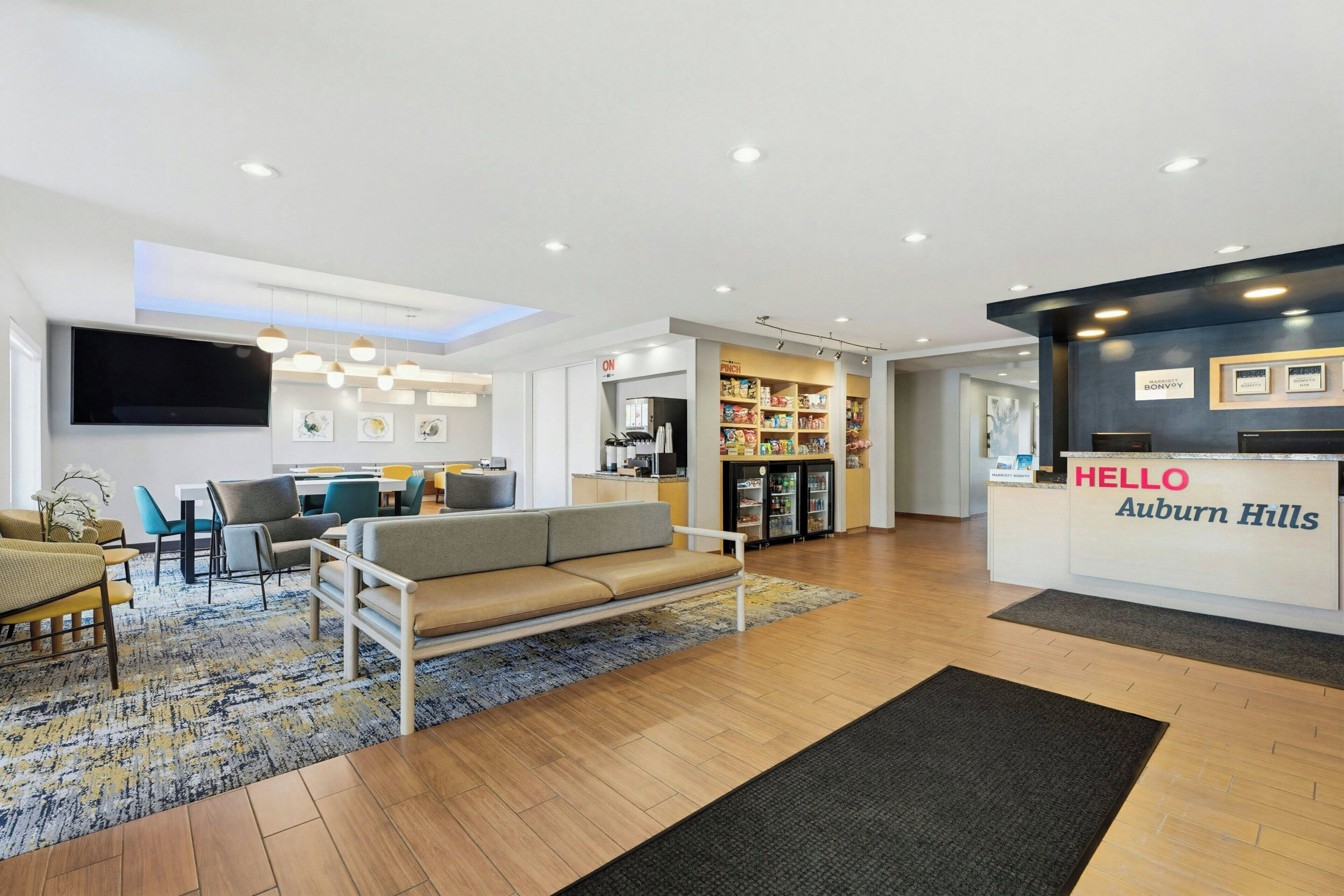 A hotel lobby with a reception desk, seating area, and a kitchenette.