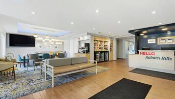 A hotel lobby with a reception desk, seating area, and a kitchenette.