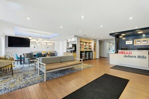 A hotel lobby with a reception desk, seating area, and a kitchenette. - TownePlace Suites Detroit Auburn Hills (Auburn Hills)