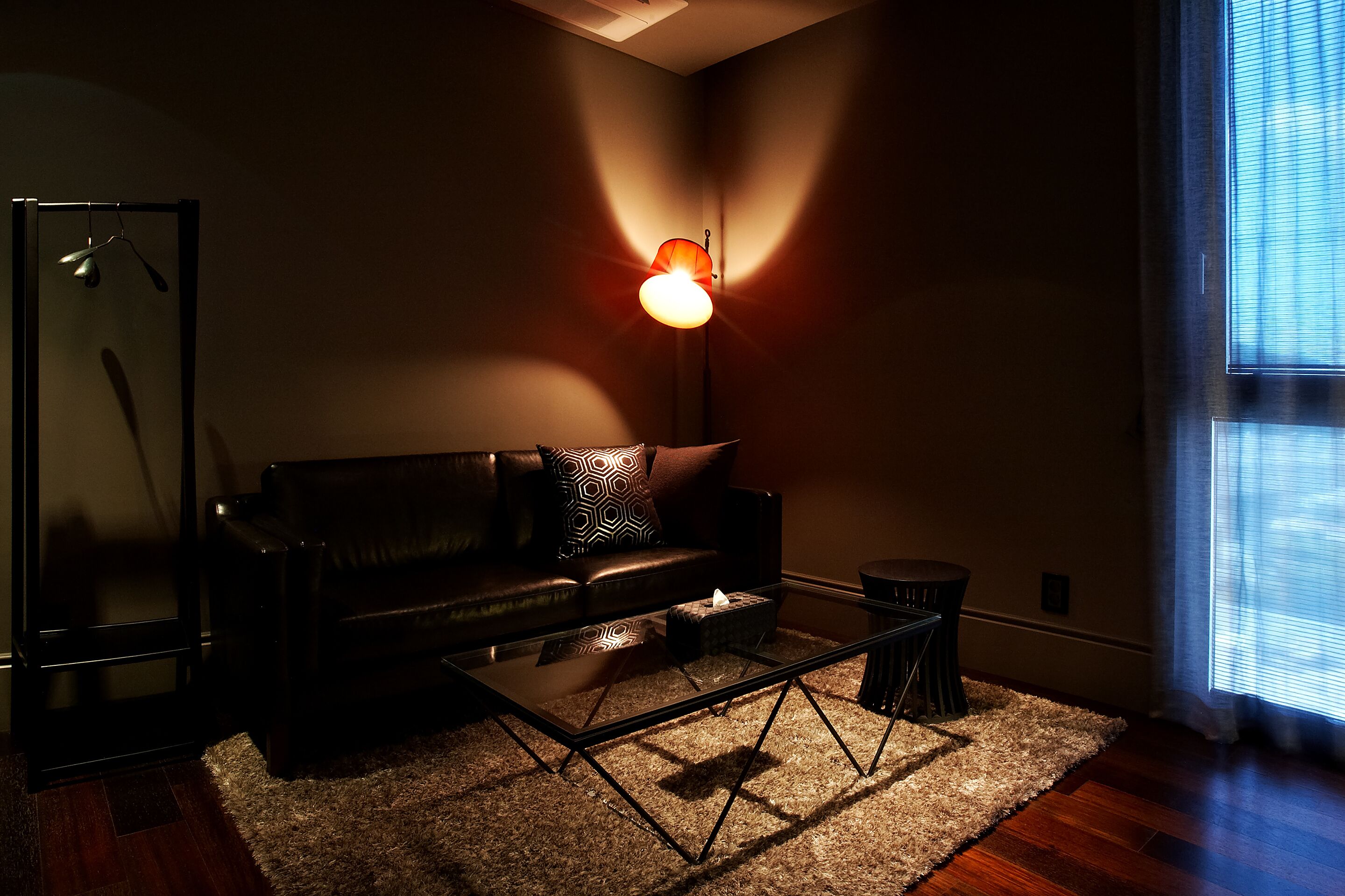 A modern living room with a black leather sofa, a glass coffee table, and a floor lamp.