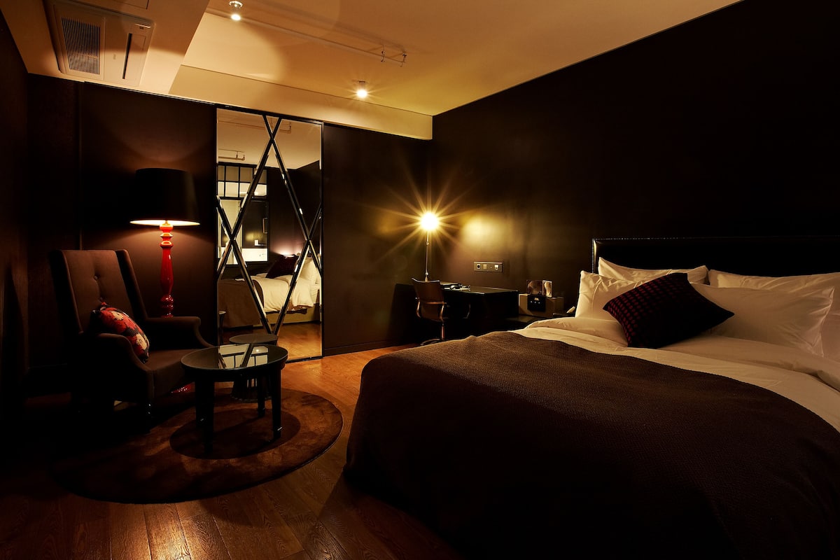 Una habitación de hotel con cama, escritorio, silla y lámpara.