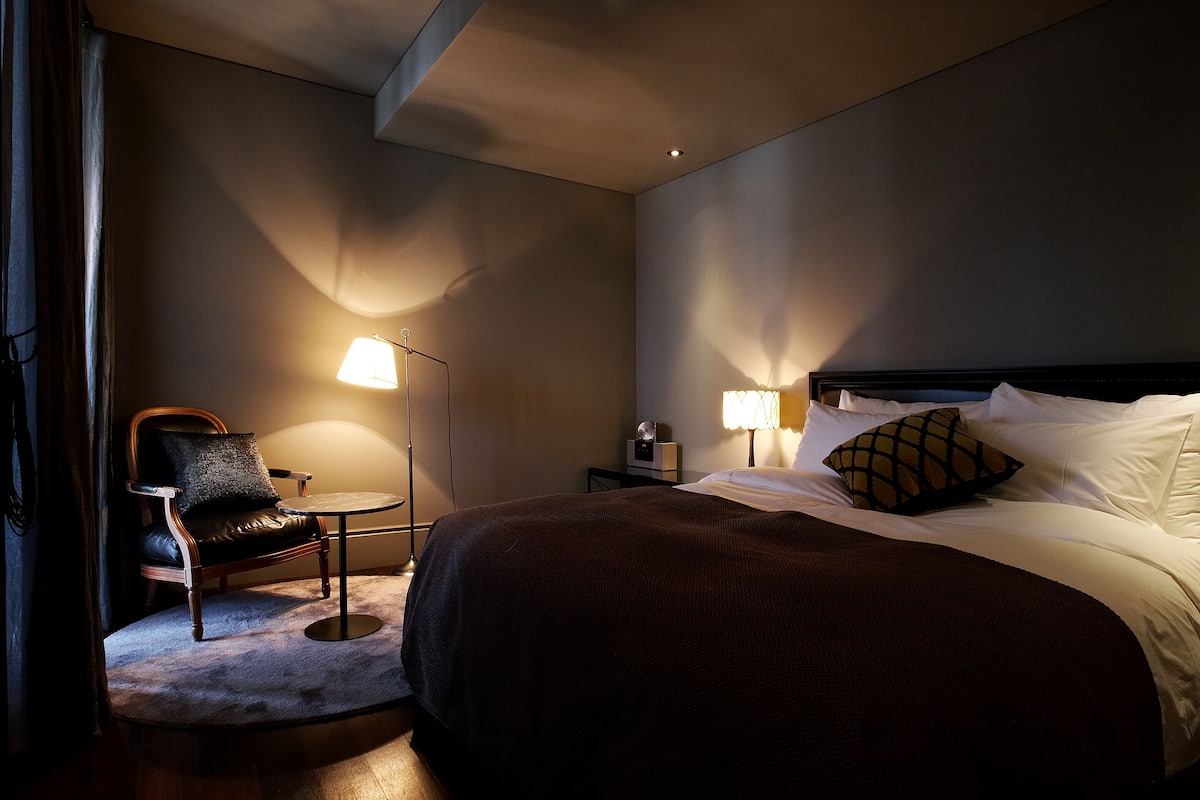 Una habitación de hotel con una cama, una silla, una mesita y dos lámparas.