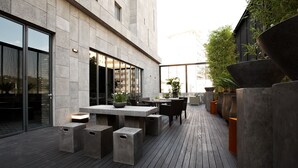 An outdoor patio with a modern design, featuring concrete tables and seating, surrounded by large planters and a wooden deck. - Lee Design Hotel (Yongin)
