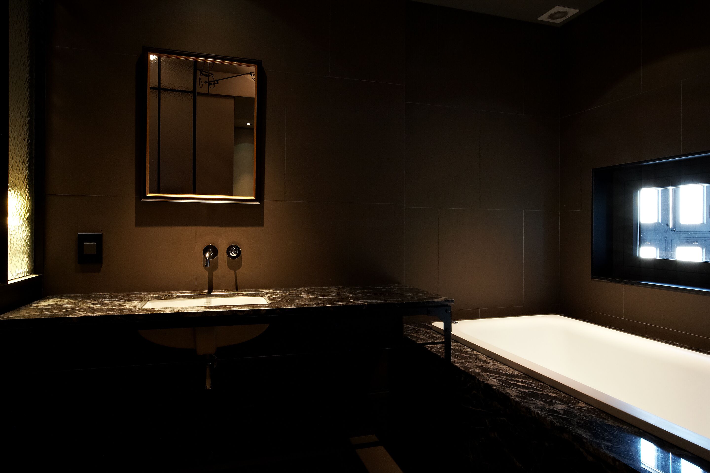 A modern bathroom with a dark marble countertop, a large mirror, and a white bathtub.