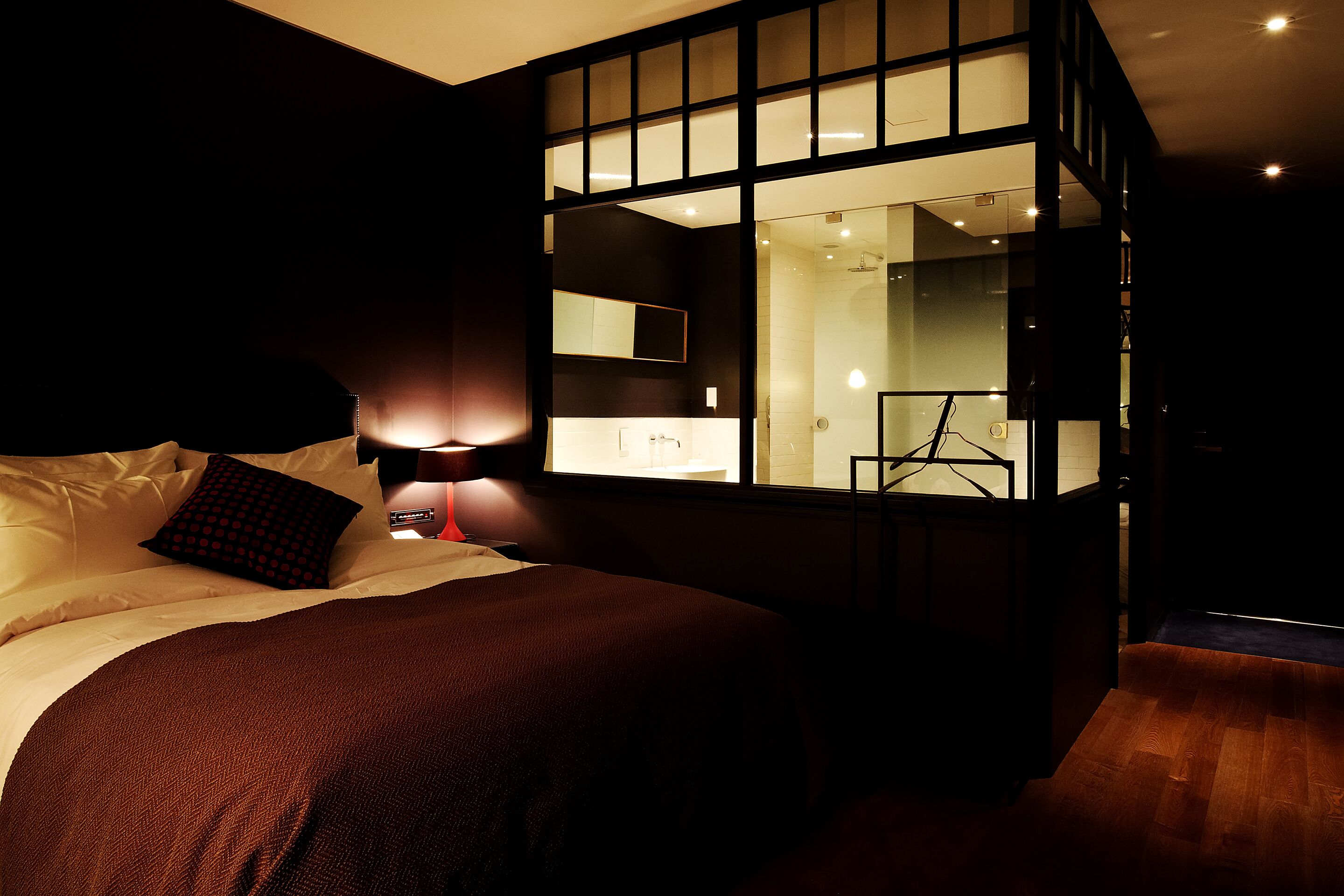 A modern bedroom with a large bed, a nightstand, a mirror, and a view of the bathroom.