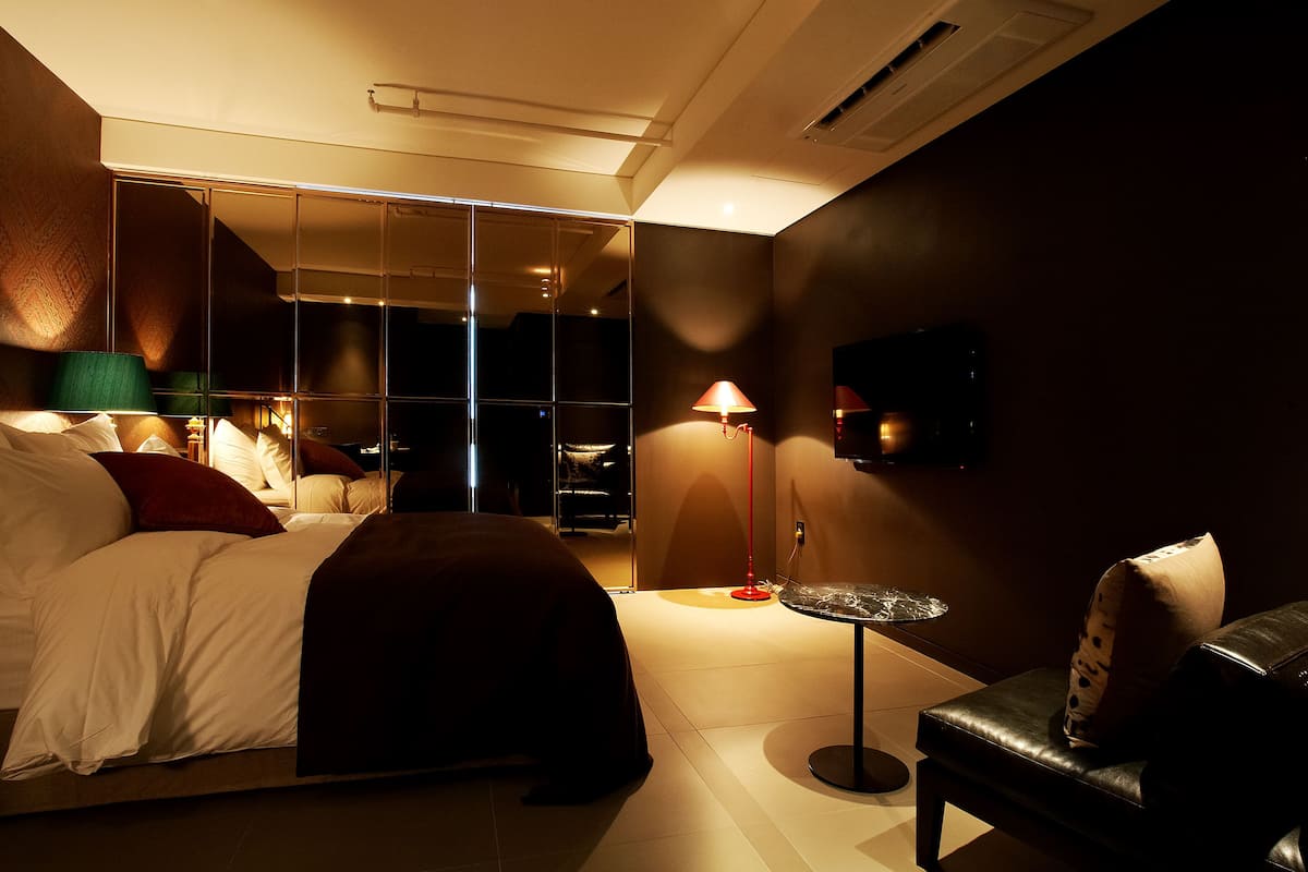 Una habitación de hotel moderna con una cama grande, una zona de estar con una pequeña mesa y un televisor montado en la pared.