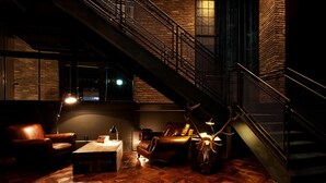 A dimly lit lounge area with a herringbone-patterned wooden floor, leather seating, and a staircase with metal railings. - Lee Design Hotel (Yongin)