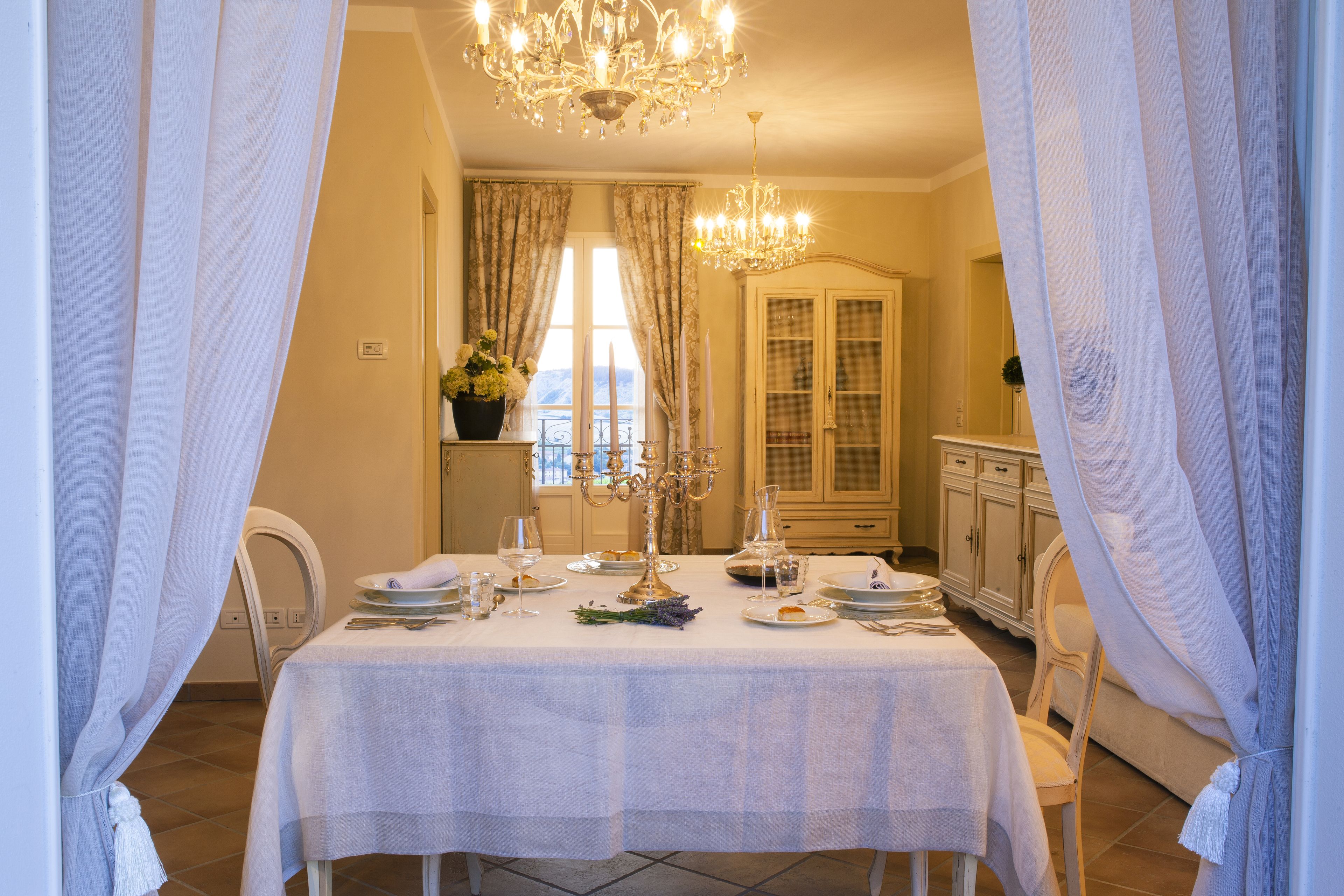A dining area with a table set for four, a chandelier, and a cabinet in the background.