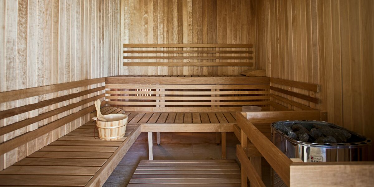 A wooden sauna with benches, a wooden table, and a bucket.