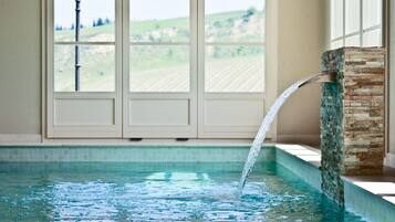 Una piscina con fuente de agua, un muro de piedra y vistas a un paisaje verde a través de amplios ventanales.
