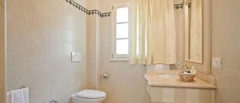 A bathroom with a toilet, bidet, sink, and a window with curtains.
