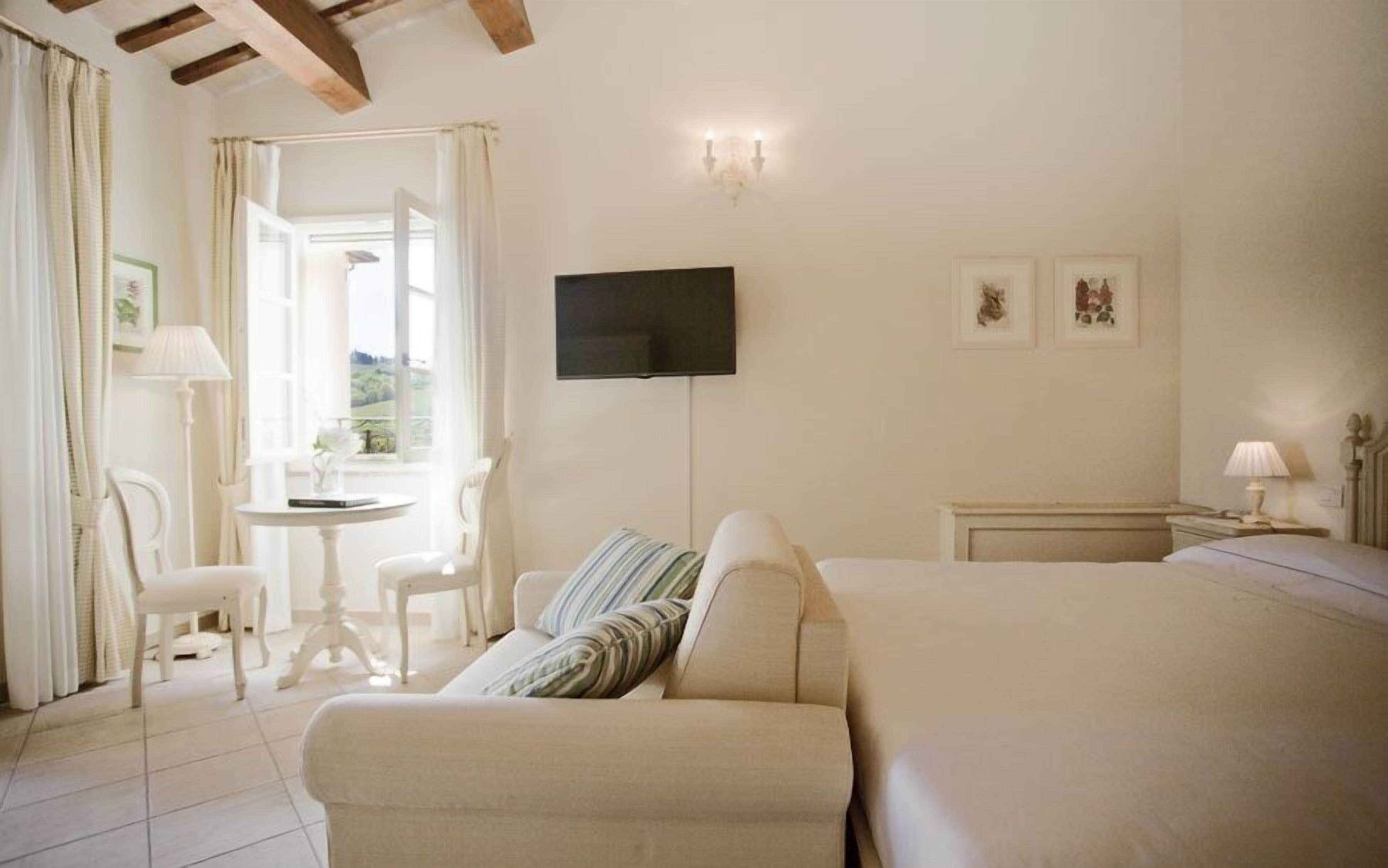 Habitación de hotel con una cama, televisión instalada en la pared, una mesita con sillas y una ventana con cortinas.
