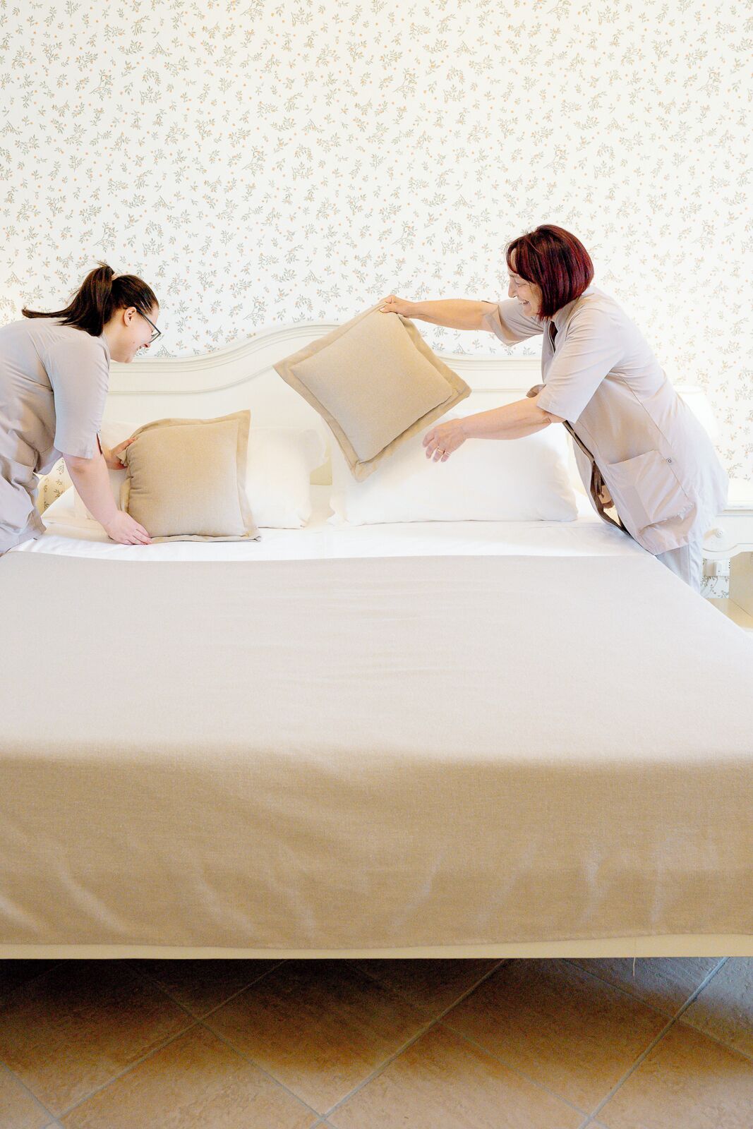 A bedroom with a bed, two pillows, and a floral wallpaper background.