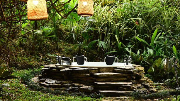 An outdoor dining area with a stone table and chairs, surrounded by lush greenery and hanging lanterns. - Finca Hotel Los girasoles (Montenegro)