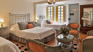 A hotel room with two beds, a sitting area with wicker furniture, a chandelier, and large windows with shutters. - Finca Hotel Los girasoles (Montenegro)