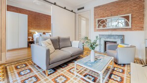 A living room with a grey sofa, a coffee table, and a fireplace. - Fuster Apartments By Aspasios  (Barcelona)