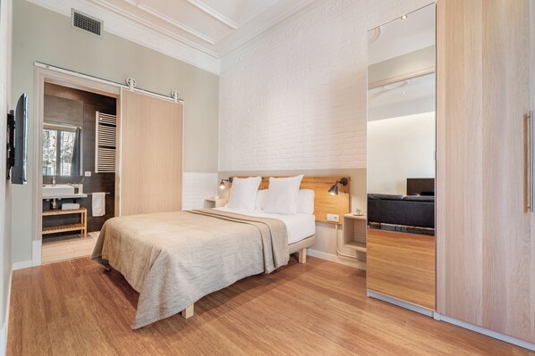 A modern bedroom with a bed, bedside tables, a wardrobe, and a bathroom with a sink and mirror. - Fuster Apartments By Aspasios (Barcelona)