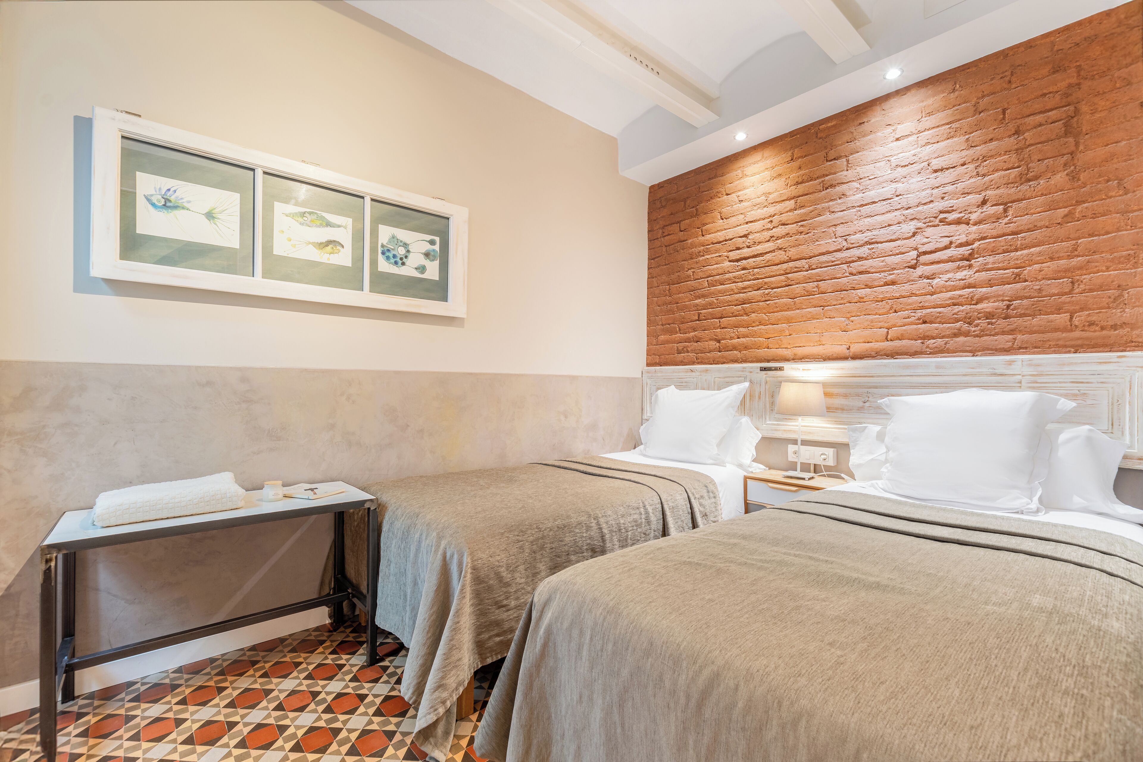 A hotel room with two beds, a small table, and a brick accent wall.