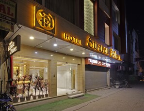 A hotel with a prominent sign, a well-lit entrance, and potted plants outside. - Hotel Swaran Palace (New Delhi)