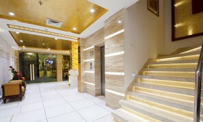 A hotel lobby with a marble staircase, a reception desk, and a view of the bar area. - Hotel Swaran Palace (New Delhi)
