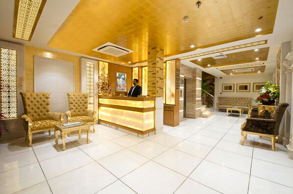 A reception area with a reception desk, two gold upholstered chairs, a coffee table, and a sofa. - Hotel Swaran Palace (New Delhi)