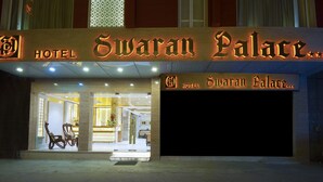 La façade de l’hôtel Swaran Palace, avec son enseigne lumineuse, un espace de réception visible à travers l’entrée et une voiture garée à l’extérieur.