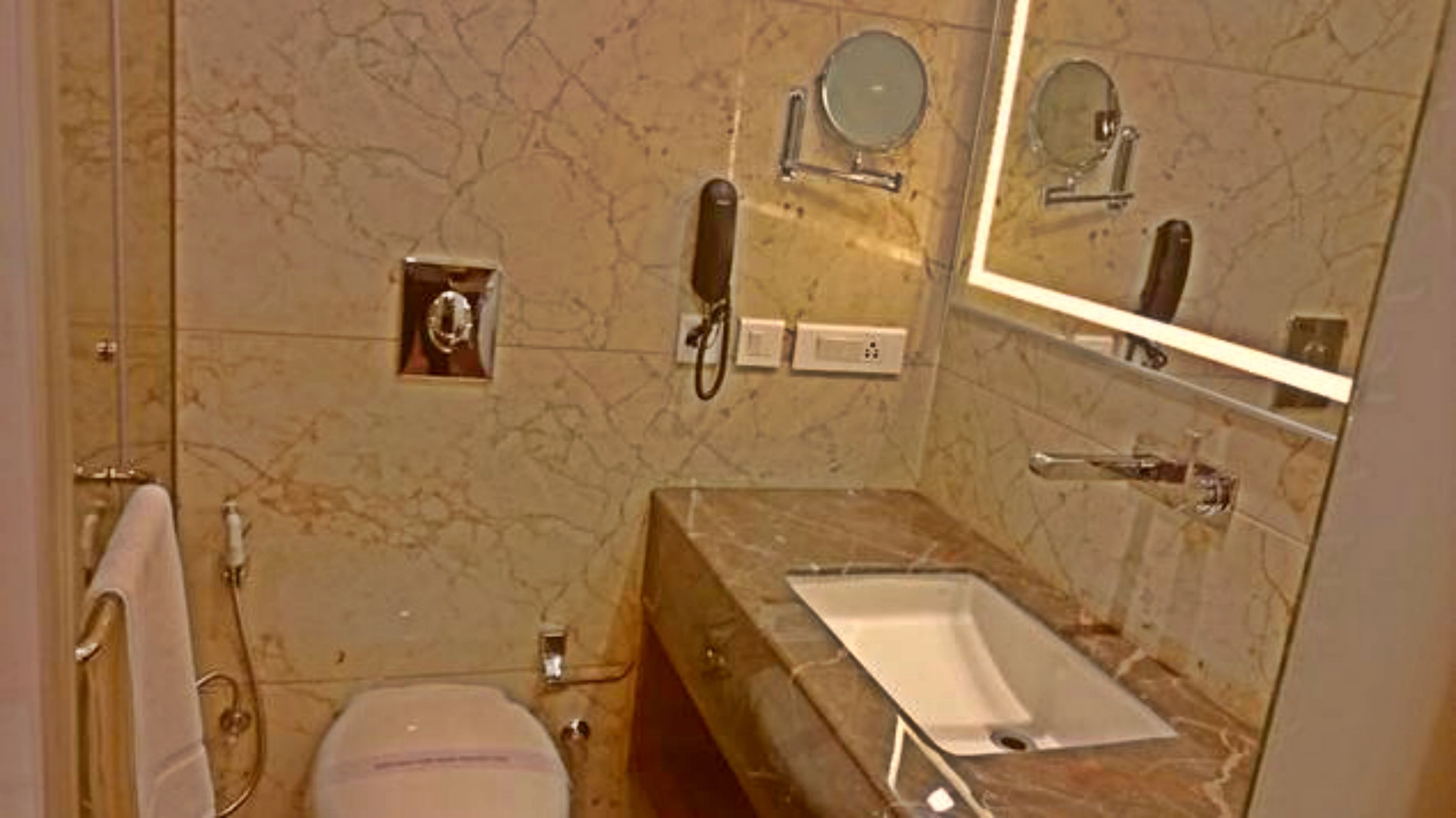 A bathroom with a marble wall, a sink, a mirror, and a toilet.