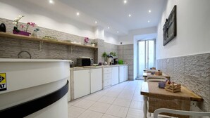 Een moderne keuken met witte kastjes, een magnetron en een spoelbak. Er zijn houten planken met decoratieve objecten en een eethoek met witte stoelen en een tafel.