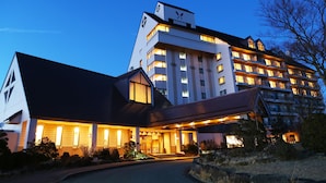 Ein mehrstöckiges Hotel mit einer markanten Uhr an der Fassade, einem gut beleuchteten Eingang und einer angelegten Auffahrt.