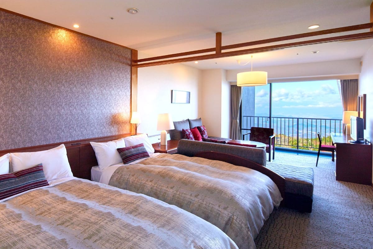 Une chambre d’hôtel avec deux lits, un balcon offrant une vue et un bureau avec une chaise.