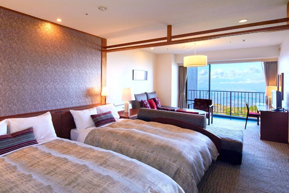 Habitación de hotel con dos camas, un balcón con vistas y un escritorio con una silla.
