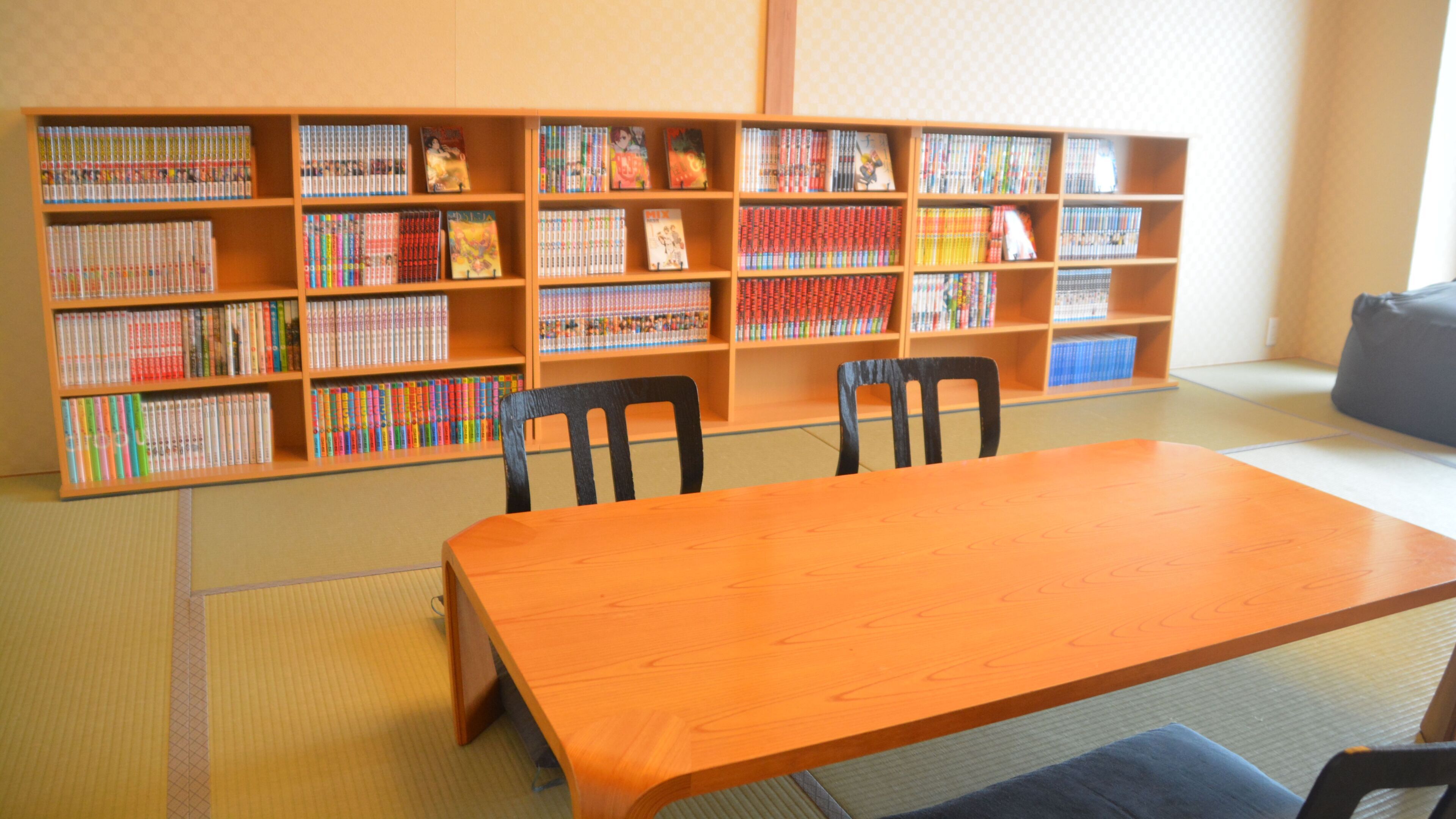 A library with wooden bookshelves, a wooden table, and black chairs.