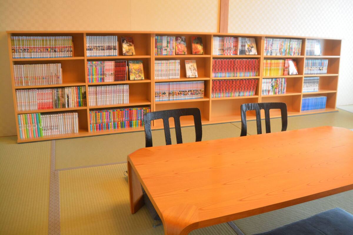 Una biblioteca con estanterías de madera, una mesa de madera y sillas negras.