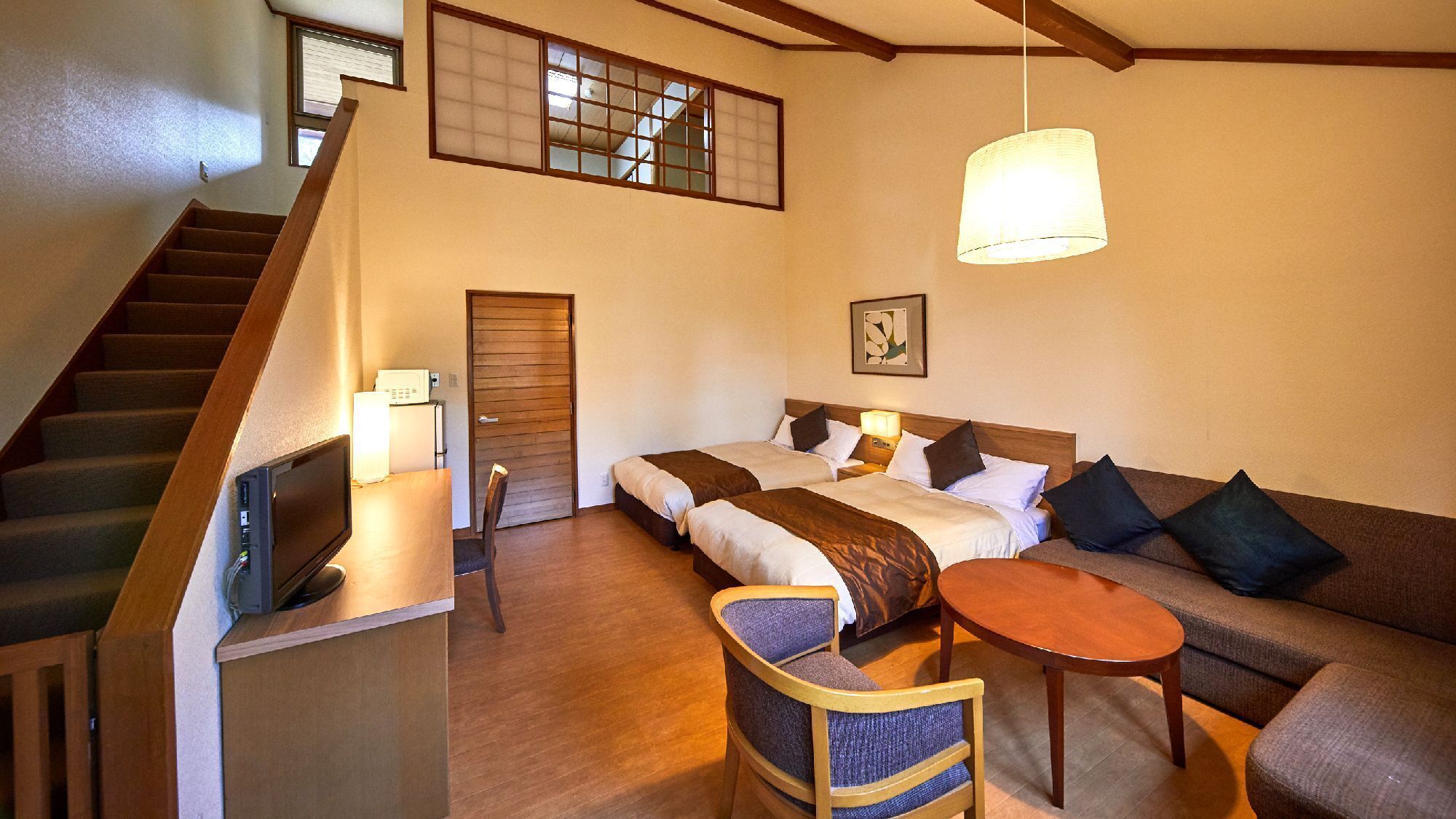 A hotel room with a staircase, two beds, a sofa, a small table, and a ceiling light.