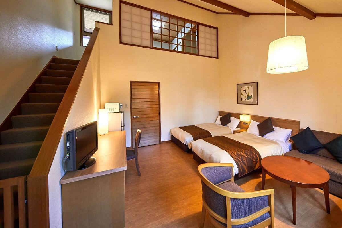 Habitación de hotel con escalera, dos camas, un sofá, una mesita y una lámpara en el techo.