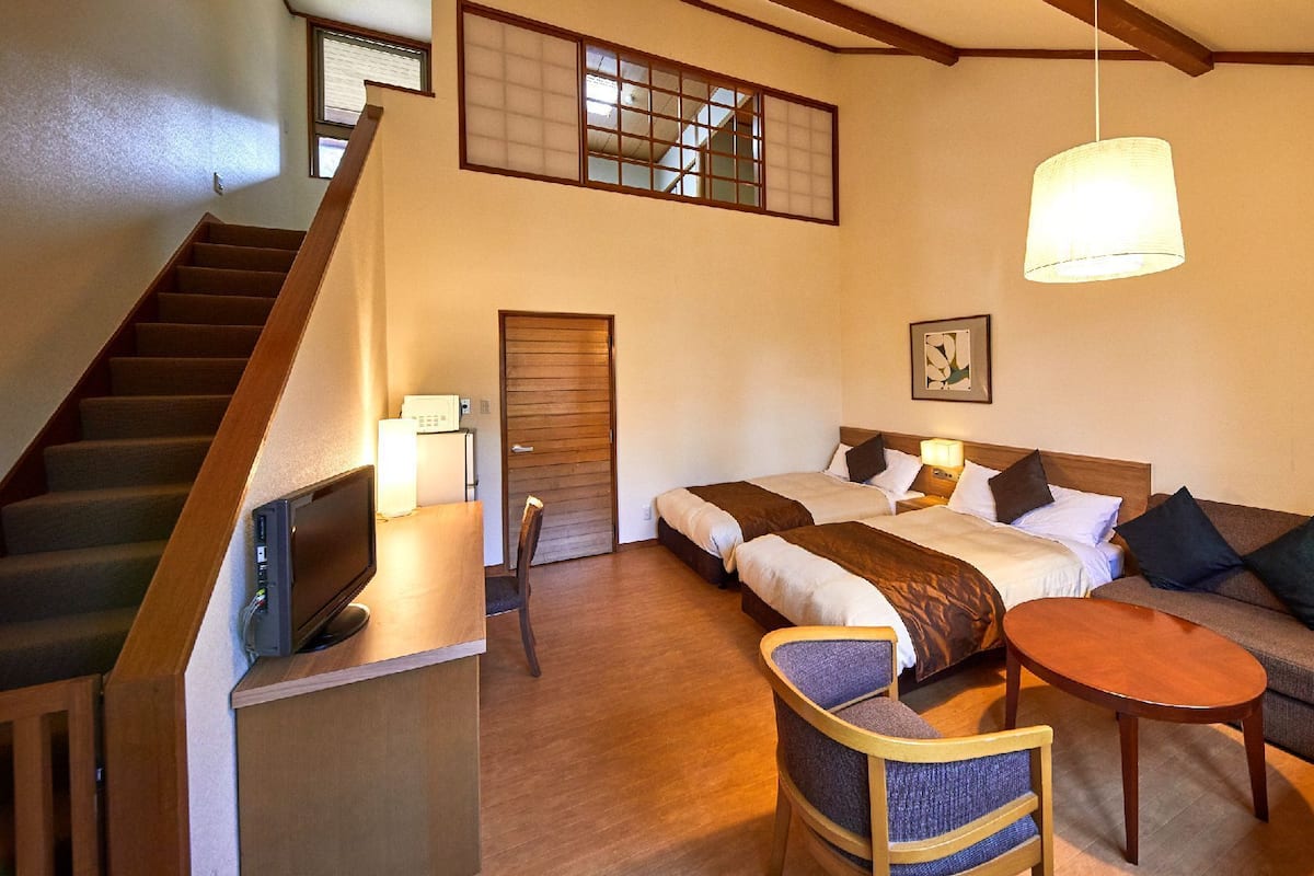 Une chambre d’hôtel avec un escalier, deux lits, un canapé, une petite table et un luminaire au plafond.
