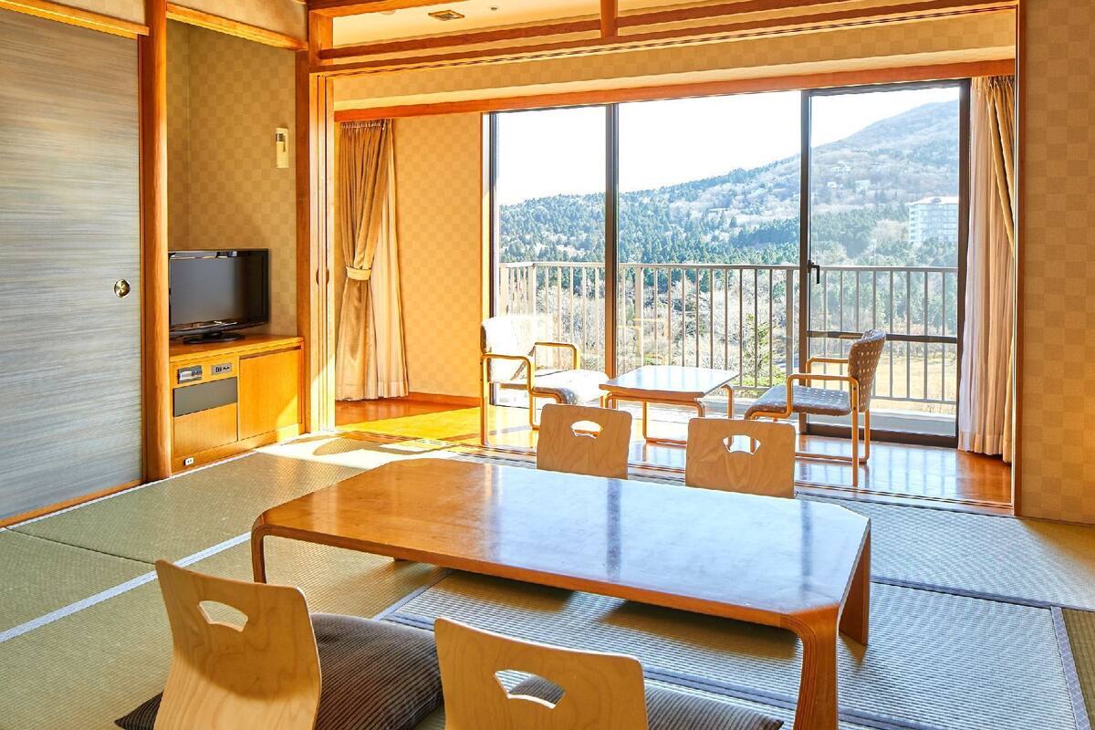 Habitación de hotel con balcón, televisor, mesa de comedor con sillas y tatamis.