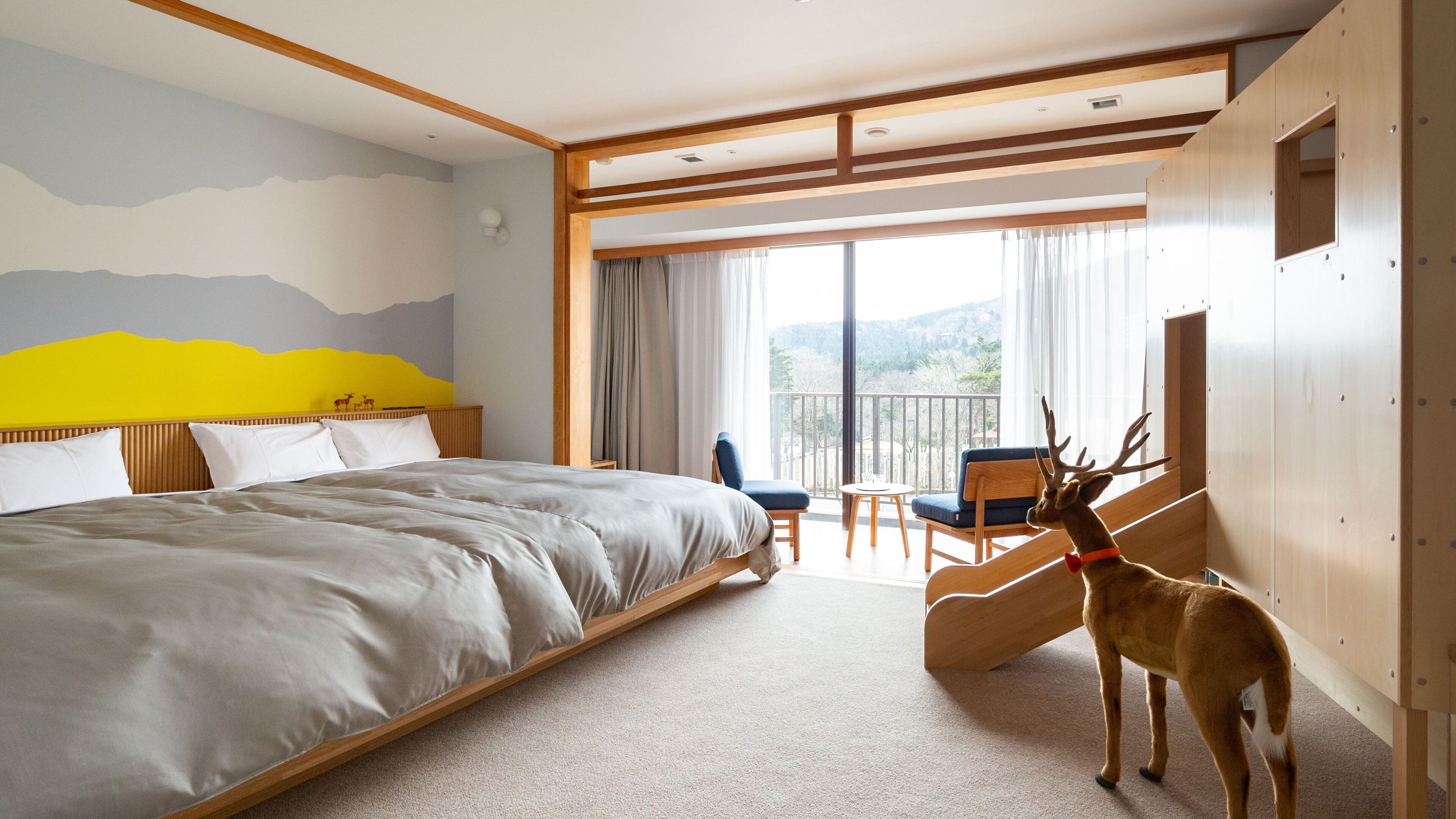 A hotel room with a large bed, a balcony with a chair, and a deer statue.