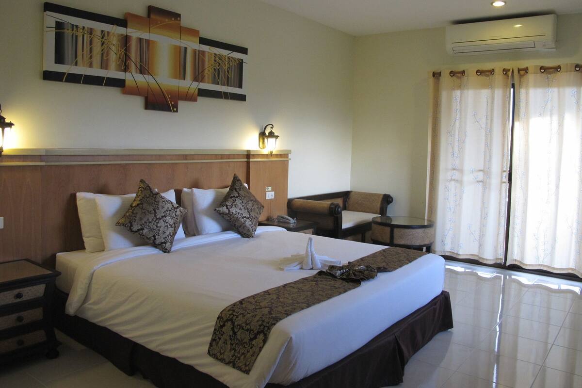 Une chambre d’hôtel avec un grand lit, une table de chevet, une chaise, une œuvre d’art accrochée au mur, un appareil de climatisation et une fenêtre avec des rideaux.