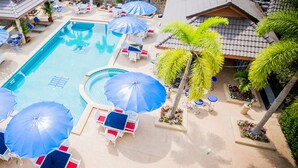 Uma piscina com guarda-sóis azuis, espreguiçadeiras brancas e palmeiras.