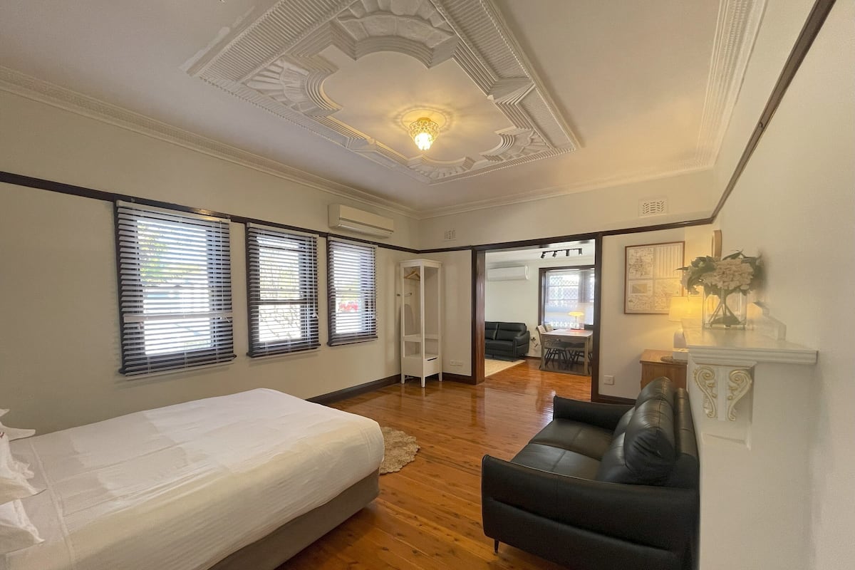 A bedroom with a bed, a black leather sofa, and a dining area with a table and chairs.