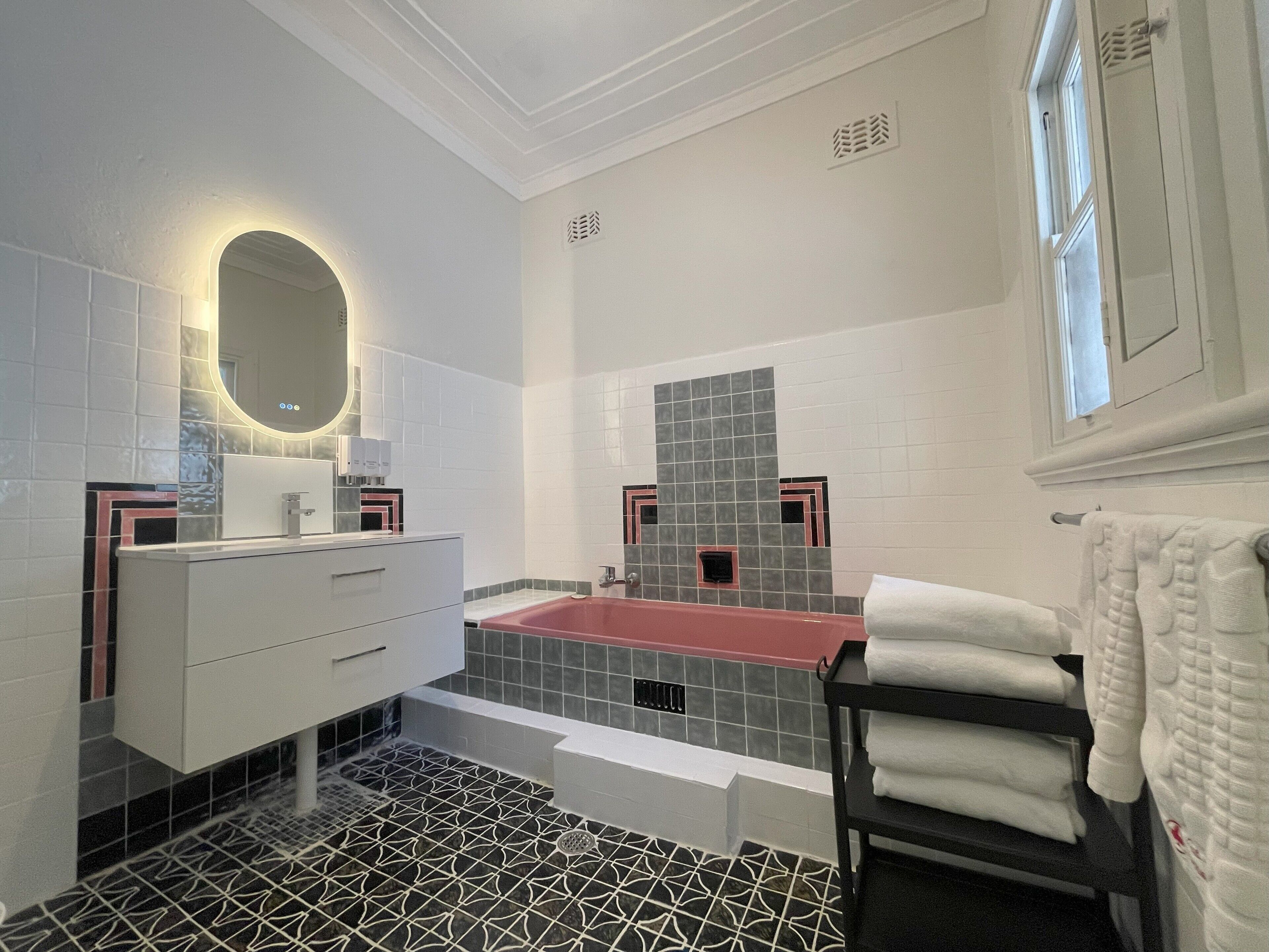A modern bathroom with a white vanity, a red bathtub, and patterned floor tiles.