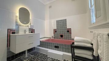 A modern bathroom with a white vanity, a red bathtub, and patterned floor tiles.
