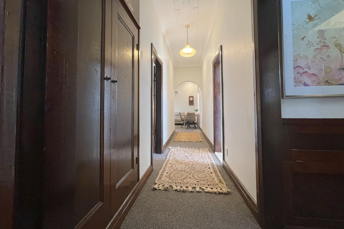 A hallway with wooden doors, a carpeted floor, a hanging light fixture, and a framed picture on the wall.